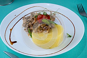 Beef cutlets meatballs with mashed potatoes on a white plate. Meat in sour cream sauce. Tomatoes and basil. Food in the