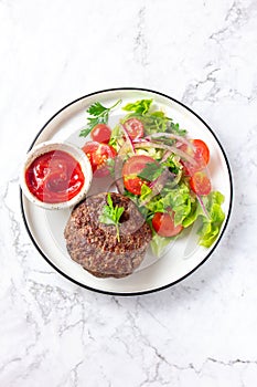Beef hamburger with lettuce tomato salad on white plate, top view