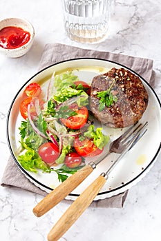 Beef hamburger with lettuce tomato salad on white plate, top view