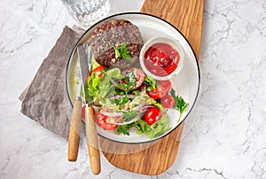 Beef hamburger with lettuce tomato salad on white plate, top view