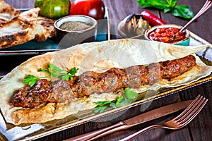 Beef kebab with pita bread, tomato sauce and vegetables on wooden background.