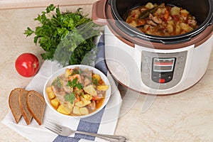 Beef, meat, stewed with potatoes, carrots, tomatoes and spices in modern multi cooker on kitchen table. Cooking stewed potatoes