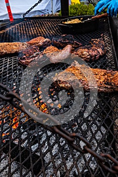 Beef pieces on smoky grill over flames with blue gloved hands