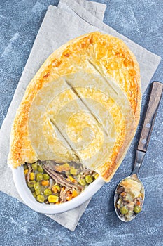Beef pot pie or deep dish pie in baking dish, crust broken open, vertical, top view