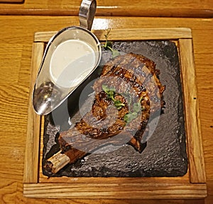 Beef shank on bones cooked on a grill. Presented on a hot stone, with baked onions and sauce