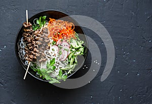 Beef skewers, rice vermicelli, pickled vegetables salad carrots, cucumbers, radishes, herbs on dark background, top view. Free spa