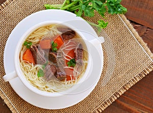 Beef soup with noodles and vegetables in soup bowl top view
