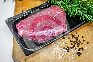 Beef steak in airtight skin packaging and spices on wooden chopping board