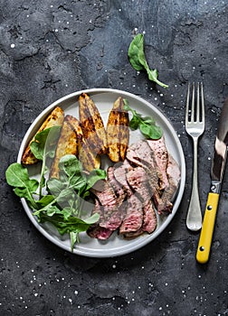 Beef steak and baked young potatoes - delicious lunch on a dark background, top view