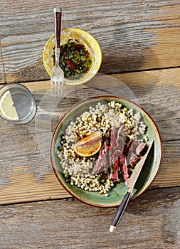 Beef steak grilled pearl barley couscous wooden table sauce water lemon top view Healthy dinner table concept