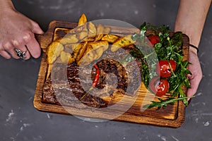 Beef steak with hot chili pepper on a wooden board with potato slices.