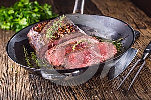 Beef steak. Juicy medium Rib Eye steak slices in pan on wooden board with fork and knife herbs spices and salt