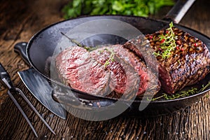 Beef steak. Juicy medium Rib Eye steak slices in pan on wooden board with fork and knife herbs spices and salt