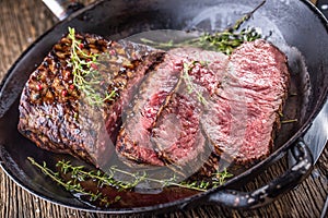 Beef steak. Juicy medium Rib Eye steak slices in pan on wooden board with fork and knife herbs spices and salt