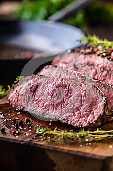 Beef steak. Juicy medium Rib Eye steak slices on wooden board with fork and knife herbs spices and salt