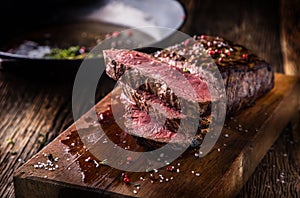 Beef steak. Juicy medium Rib Eye steak slices on wooden board with fork and knife herbs spices and salt