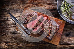 Beef steak. Juicy medium Rib Eye steak slices on wooden board with fork and knife herbs spices and salt