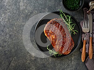Beef Steak medium rare on black plate, surfed with tableware on black stone table with ample copy space. Dark background.