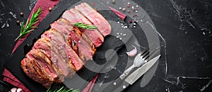 Beef steak and rosemary on a slate board. Roast beef medium rare. Black stone background. Top view, flat lay, banner.