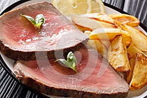 Beef steak is served with roasted potatoes and lemon close-up on