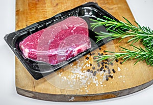Beef steak in vacuum skin packaging and spices on wooden chopping board
