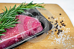 Beef steak in vacuum skin packaging and spices on wooden chopping board