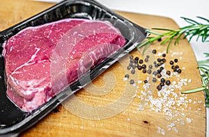 Beef steak in vacuum skin packaging and spices on wooden chopping board with copyspace