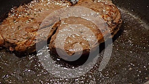 Beef steaks are cooking in the pan, turning meat with tongs