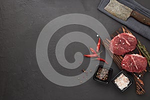 Beef steaks on cutting board and spices on black slate background. Top view. Steak menu