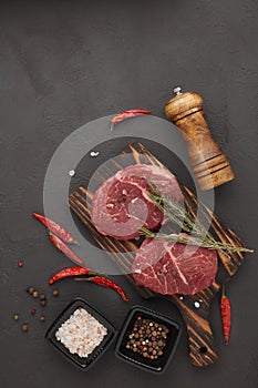 Beef steaks on cutting board and spices on black slate background. Top view. Steak menu