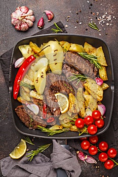 Beef steaks grilled with baked potatoes and vegetables in a pan