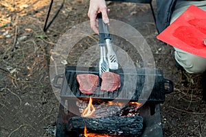 Beef steaks grilling on a cast iron plate on a camp fire. Campfire cooking.