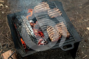 Beef steaks grilling on a cast iron plate on a camp fire. Campfire cooking.