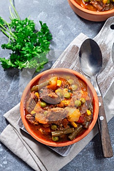 Beef stew with potato, green beans, carrot, peas and corn, in ceramic bowl, vertical, top view