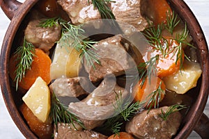 Beef stew with vegetables and herbs in a pot macro top view.