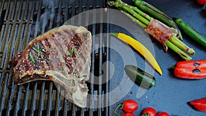 Beef T-Bone steak on the cooking grill with grilled vegetables. Slow motion