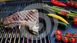 Beef T-Bone steak on the cooking grill with grilled vegetables. Slow motion. Close up