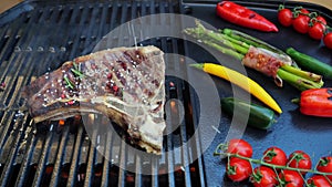 Beef T-Bone steak on grill sprinkle with spices, salt, peppercorns and rosemary, grilled vegetables. Slow motion. Close up