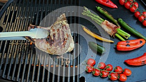 Beef T-Bone steak grill turn over on barbecue, grilled vegetables.