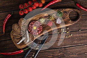 Beef Tartar with a raw egg yolk, capers, rye bread and chilis on a wooden board with spoon and fork flat lay. Shot made from above