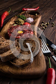 Beef Tartar with a raw egg yolk, capers, rye bread and chilis on a wooden board with spoon and fork. Shot made from above on a