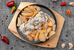 Beef tongue in creamy mushroom sauce. With baked potatoes in a rustic way. In a cast-iron pan with a wooden stand. View from above