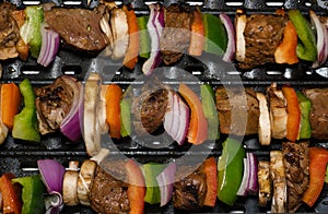 Beef and vegetable shish kebabs cooking on a grill.