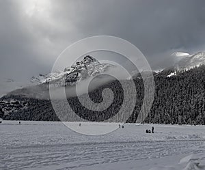 Beehive and Devils Thunb watch over ice skaters with clouds rolling by. Lake Louise. Banff National Park Alberta Canada