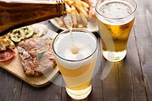 Beer being poured into glass with gourmet steak and french fries