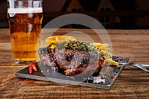 Beer being poured into glass with gourmet steak and french fries on wooden background.