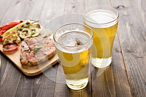 Beer being poured into glass with steak on wooden background