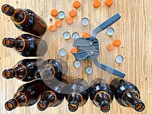 Beer brewing at home, plastic capper to put metal caps on bottles, brown glass beer bottles and orange crown caps on wooden