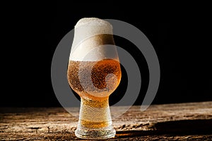 Beer. Cold Craft light Beer in a glass with water drops on the wooden table over the black background