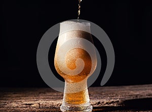 Beer. Cold Craft light Beer in a glass with water drops on the wooden table over the black background